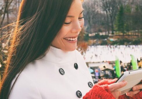 Woman walking happy in Central park, New York City in winter with Wollman skating rink using tech device smart phone tablet app for directions, tourist guide. Candid smiling -girl on Manhattan, USA.